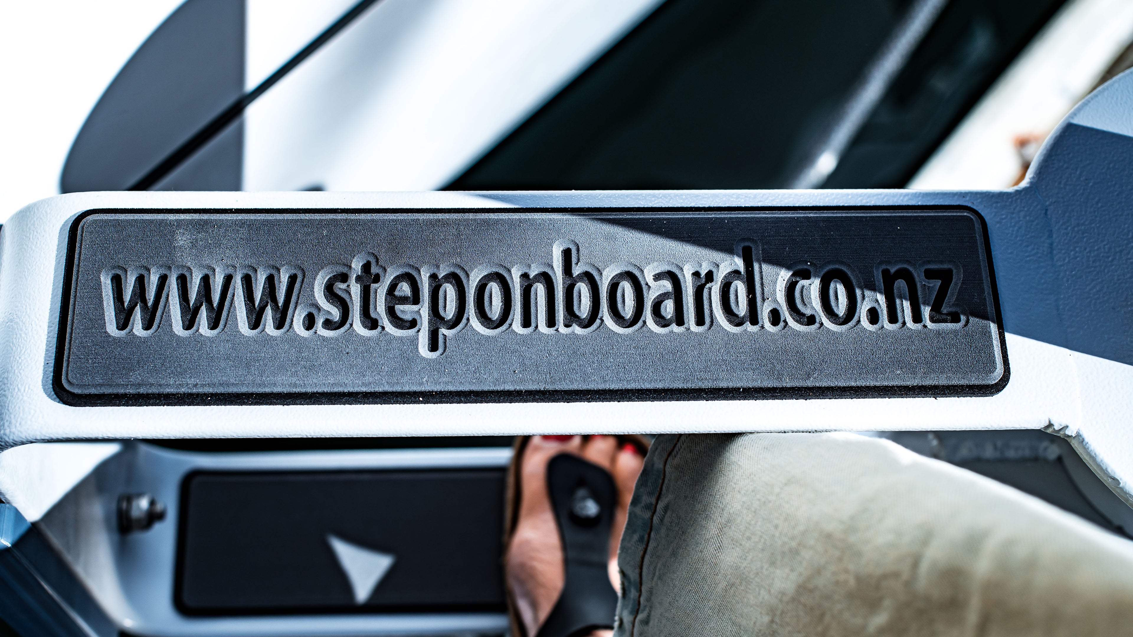Metallic step plate with 'www.steponboard.co.nz' text on a vehicle, with a blurred background.